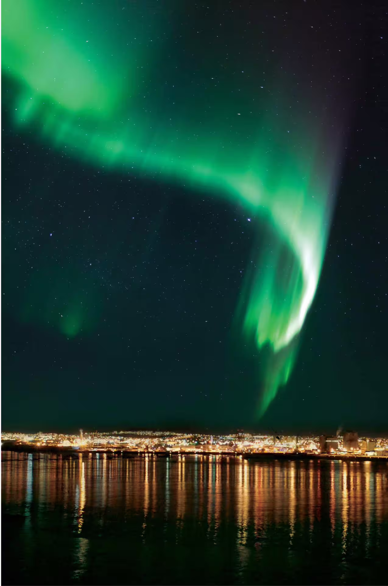 Brilliant green northern lights aurora borealis over illuminated Reykjavik waterfront at night