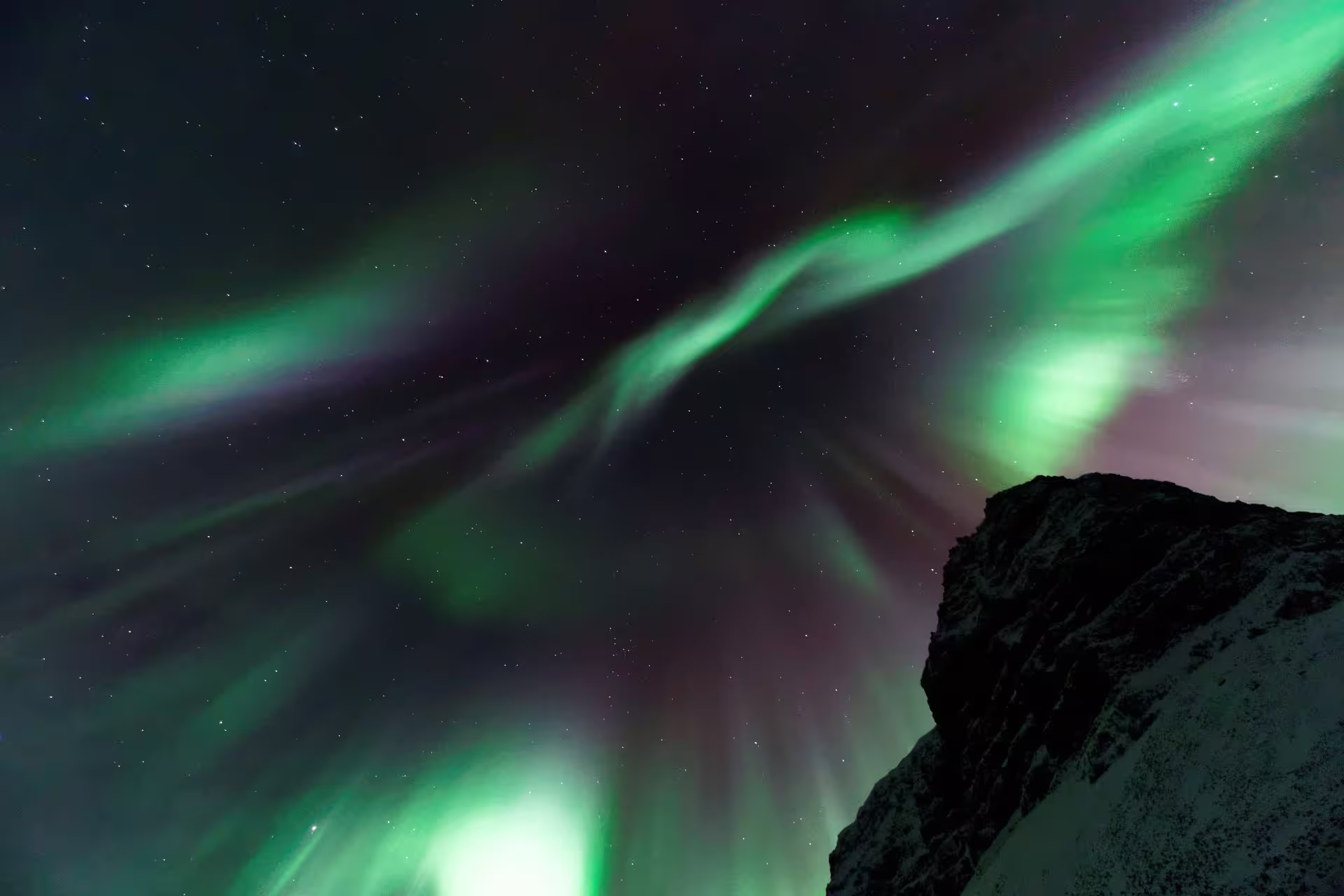 Vibrant green aurora borealis dancing over a rocky snowy cliff in Reykjavik Iceland night sky