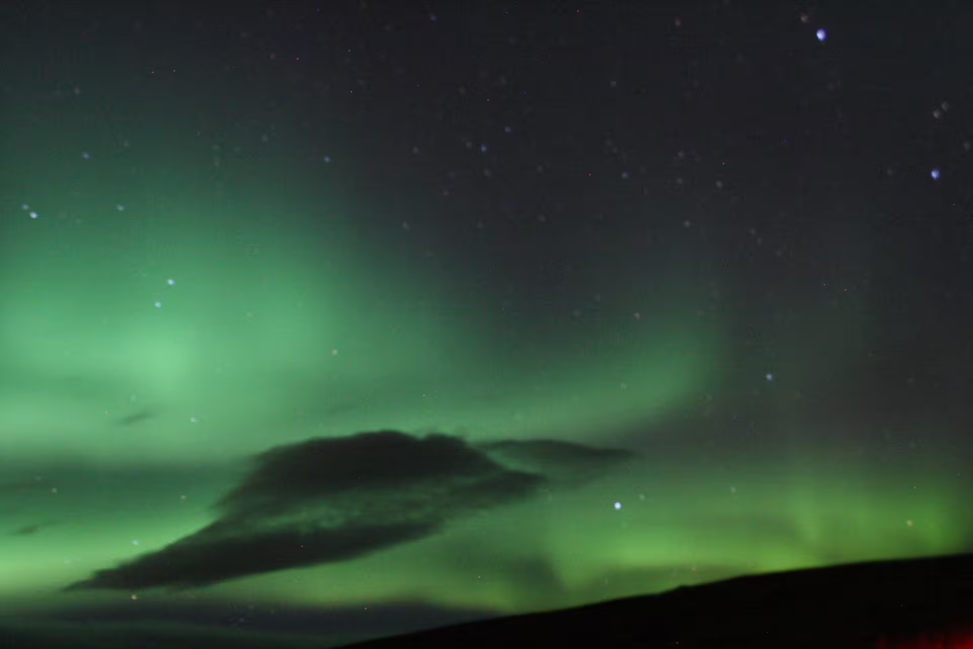 Vibrant green northern lights aurora borealis over dark clouds and starry night sky in Iceland