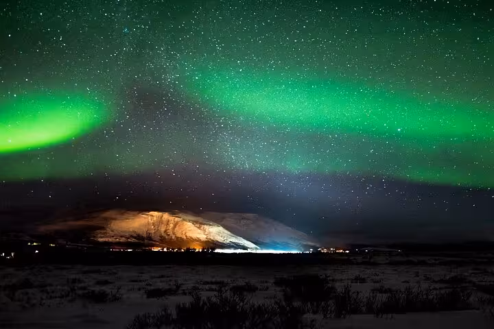 Vivid green northern lights aurora borealis over snow-covered mountain near Reykjavik Iceland at night