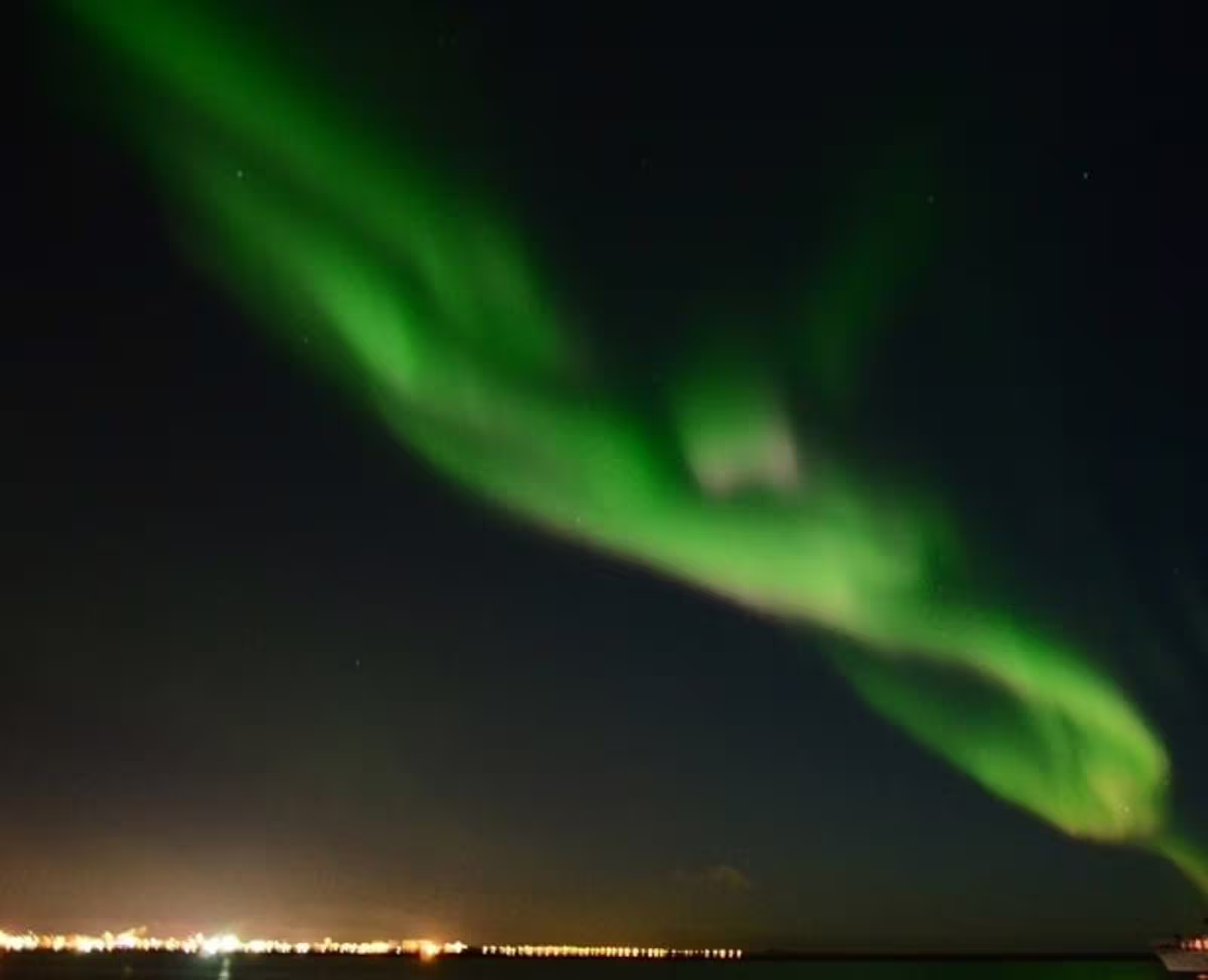 Vivid green aurora borealis swirling over Reykjavik city lights at night