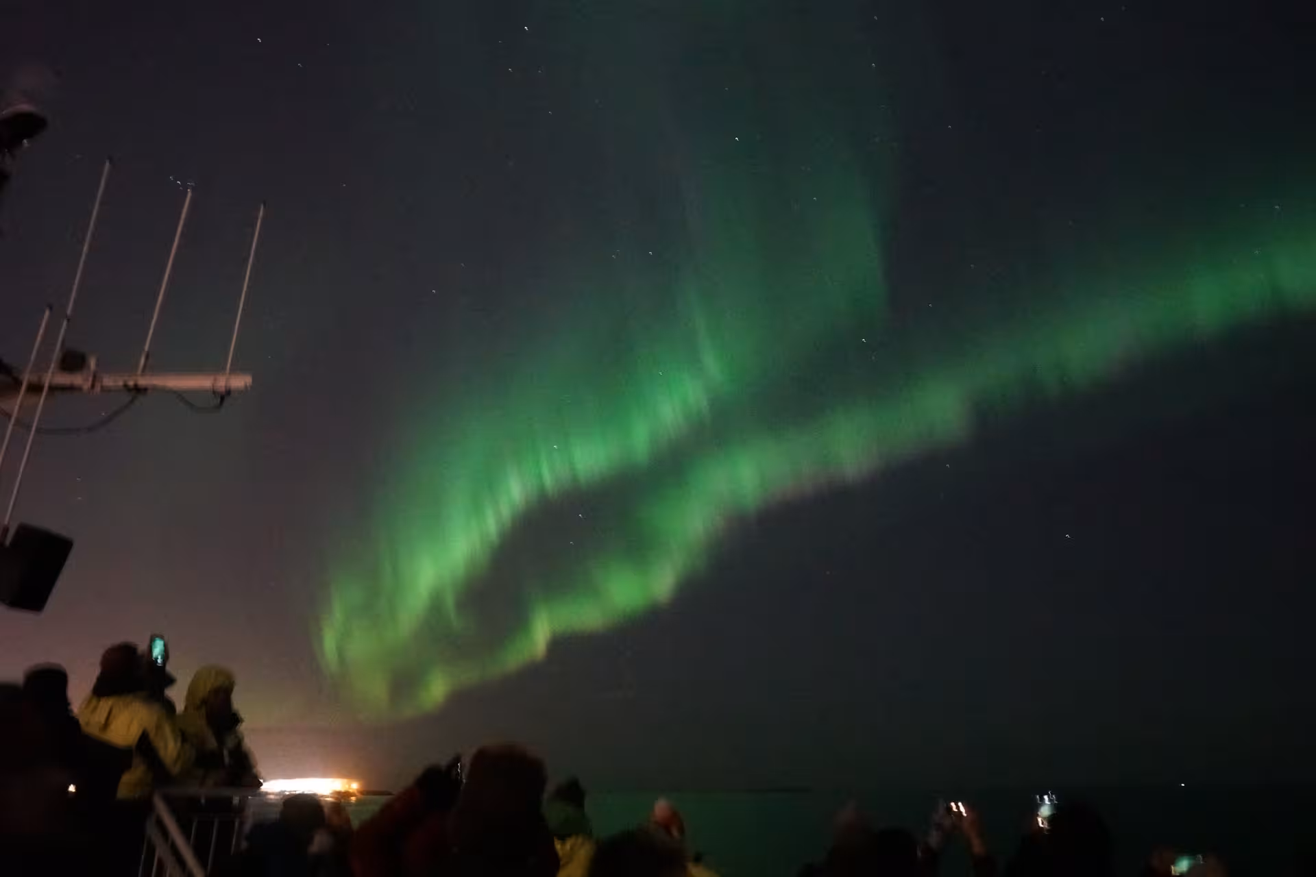 Green Northern Lights glowing in the night sky above a boat tour in Iceland