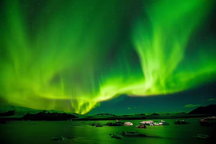 Vibrant green northern lights aurora borealis reflecting over icy lagoon in Reykjavik night sky