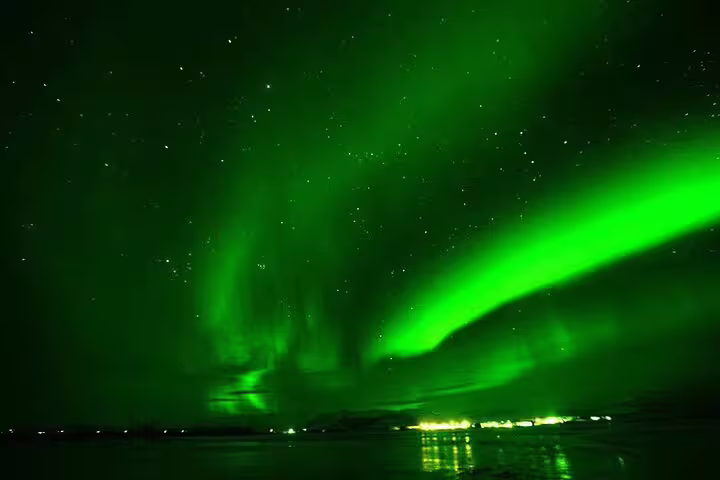 Vibrant green northern lights aurora borealis dancing over Reykjavik waters at night