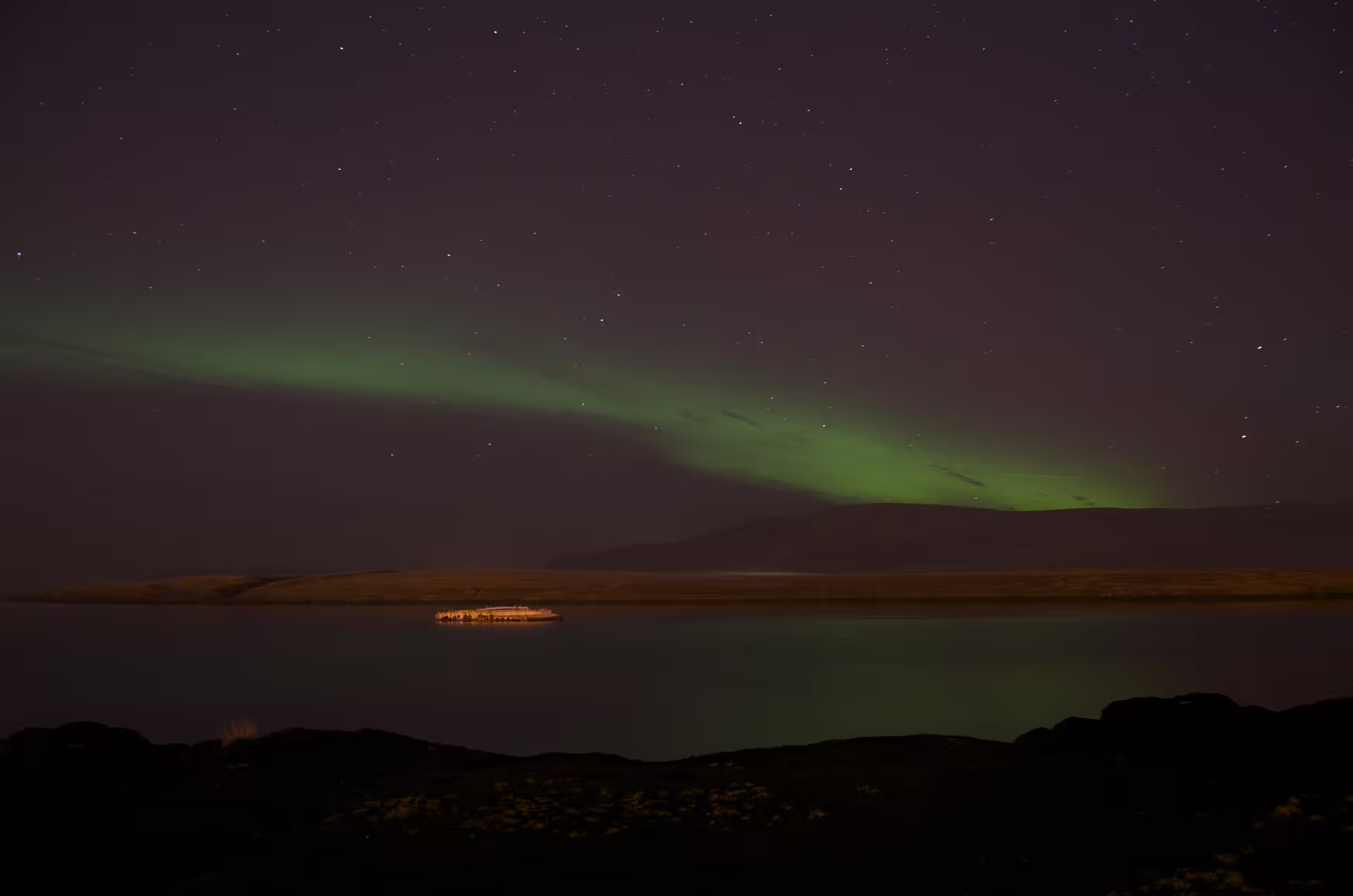 Northern lights aurora borealis arc over calm fjord waters near Reykjavik at night