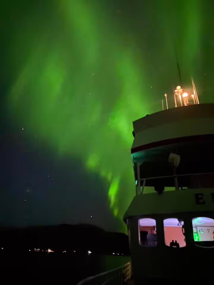 Northern lights aurora borealis over a boat on Reykjavik Bay at night with green glowing sky