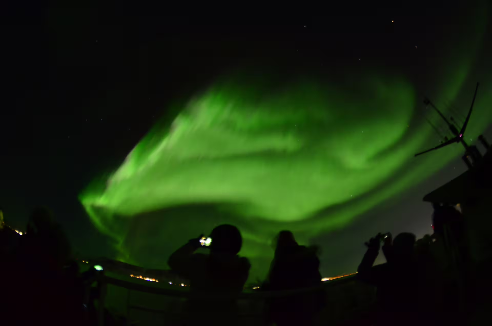 Silhouettes of tourists photographing vivid green northern lights aurora borealis from a boat in Reykjavik Bay