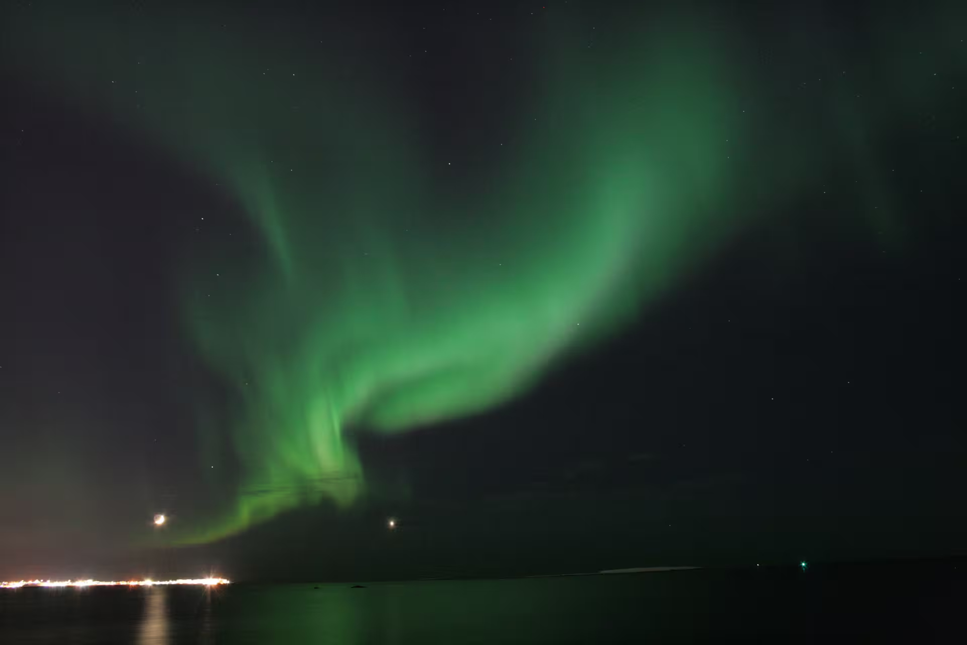 Vivid green aurora borealis swirling over calm ocean waters near Reykjavik Iceland at night