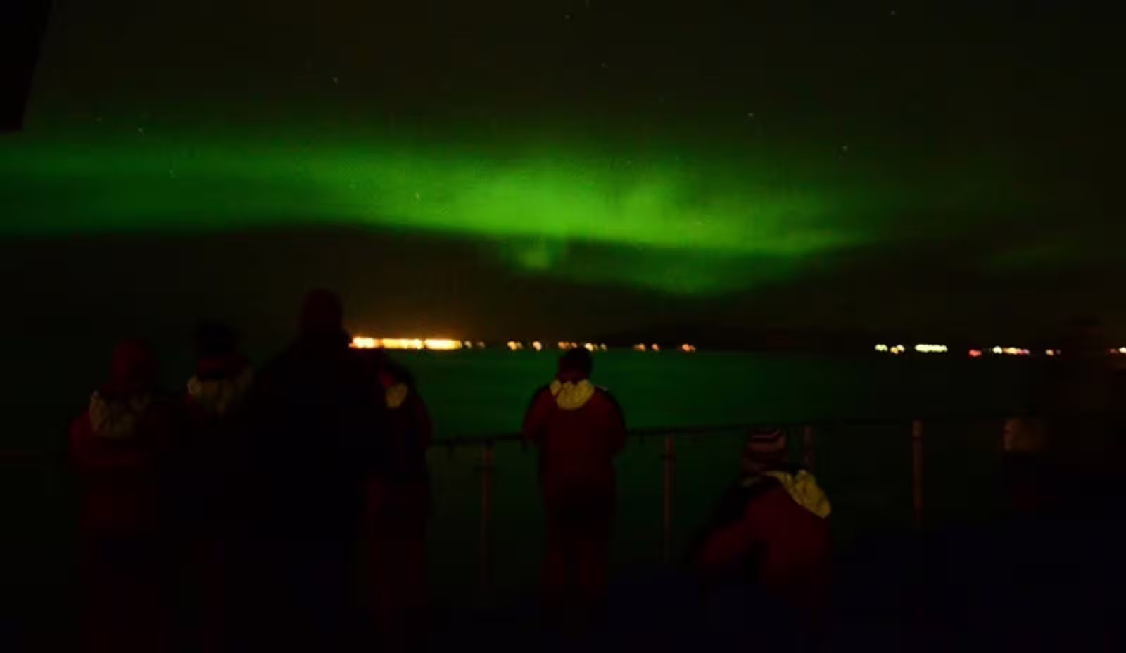 Tourists watching vivid green northern lights aurora from a boat deck at night in Reykjavik Iceland