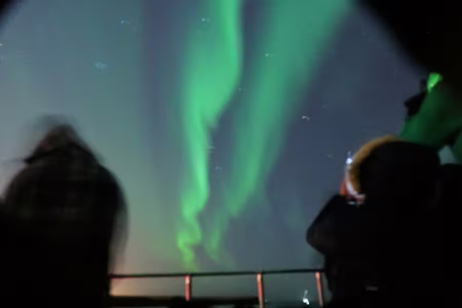 Tourists watching vibrant green northern lights aurora borealis from a boat deck in Reykjavik at night