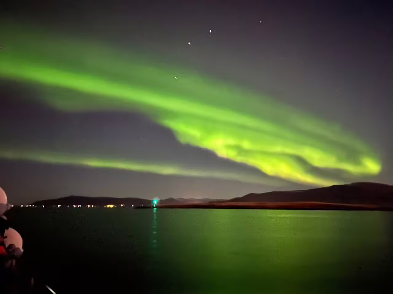 Vibrant green northern lights aurora borealis dancing over calm ocean waters on a night boat tour from Reykjavik