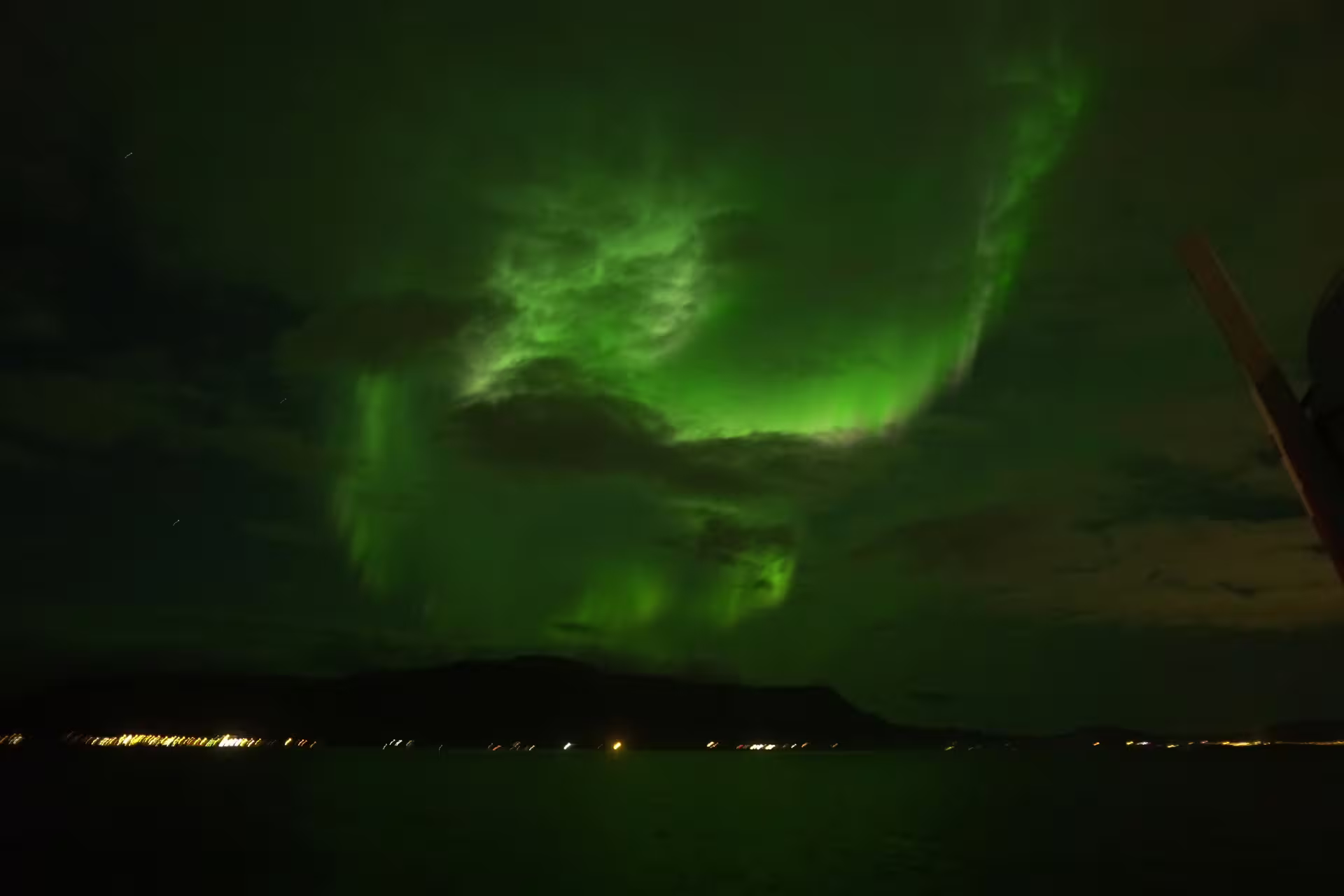 Vibrant green aurora borealis swirling over dark ocean waters near Reykjavik Iceland at night