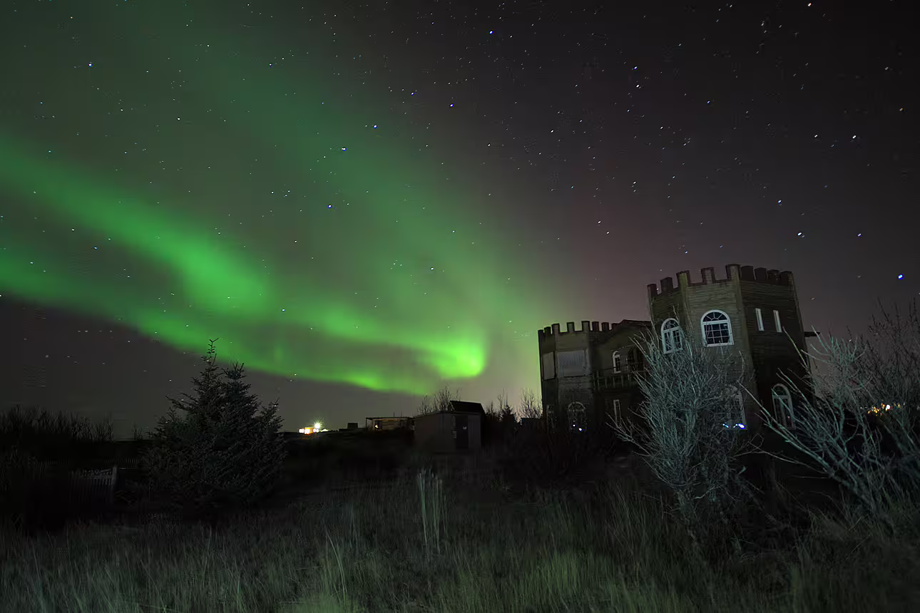 Aurora borealis green northern lights dancing over a castle-like building in Iceland at night