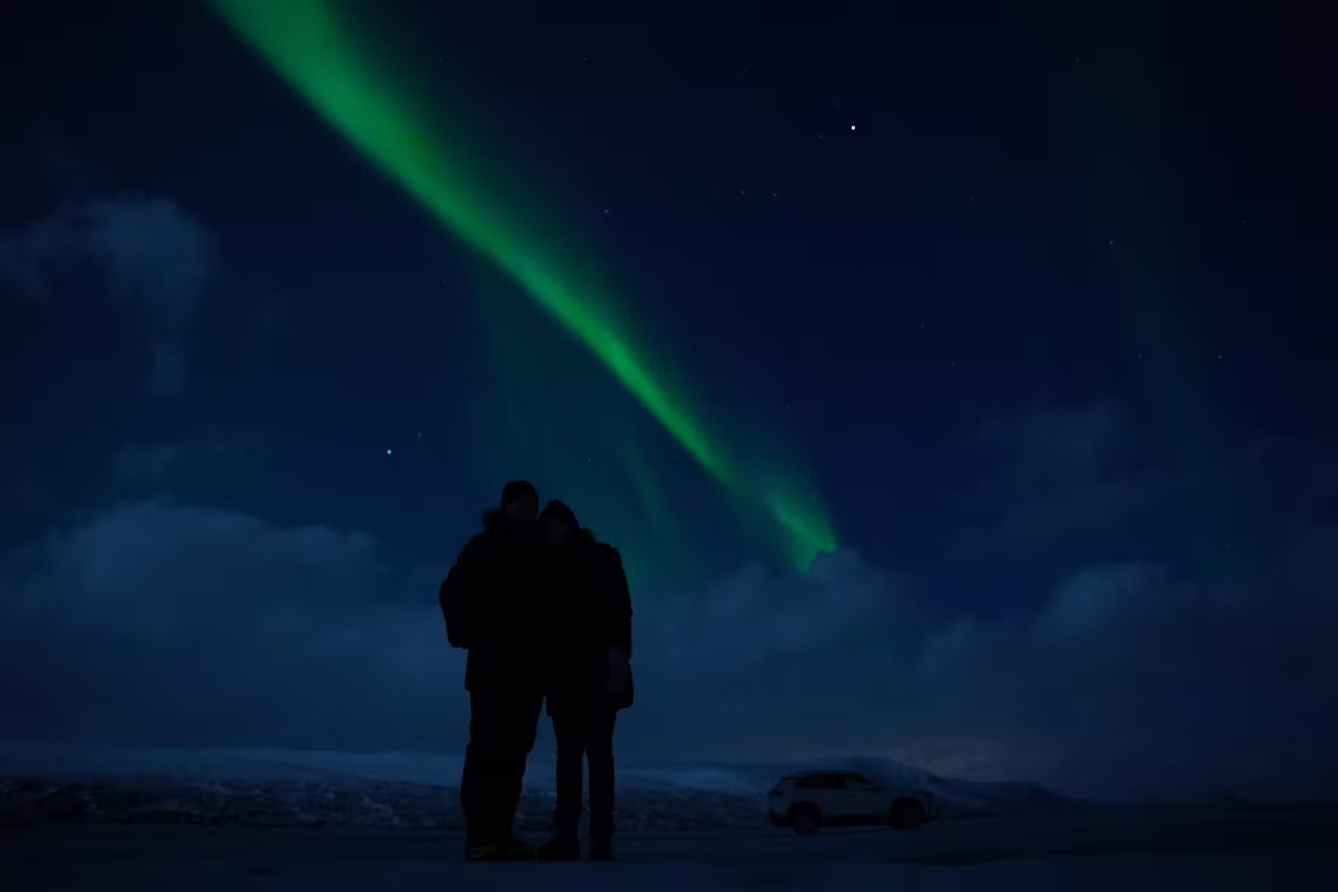 Couple silhouetted under vibrant green northern lights in snowy Iceland night sky