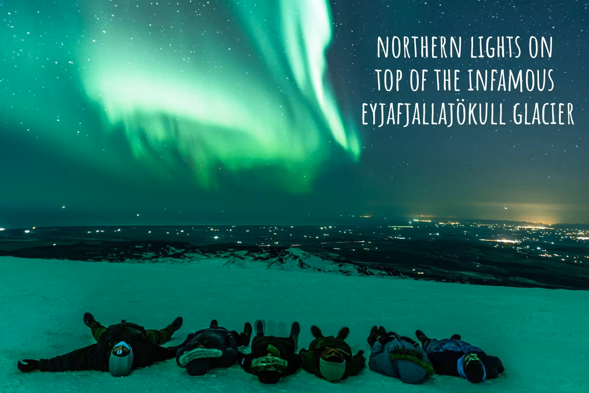 Group lying on Eyjafjallajökull glacier watching vibrant green northern lights over Iceland at night