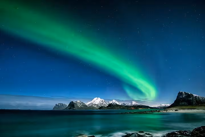 Aurora borealis northern lights swirling over snowy mountains and calm Arctic fjord at night