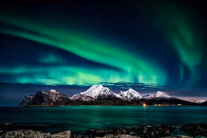 Vivid green northern lights aurora dancing over snow-capped mountains reflected in calm Arctic waters at night