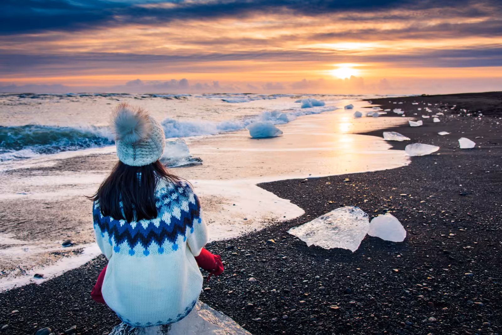 Individual in warm attire gazes at vibrant sunset over icy beach during Northern Lights adventure.