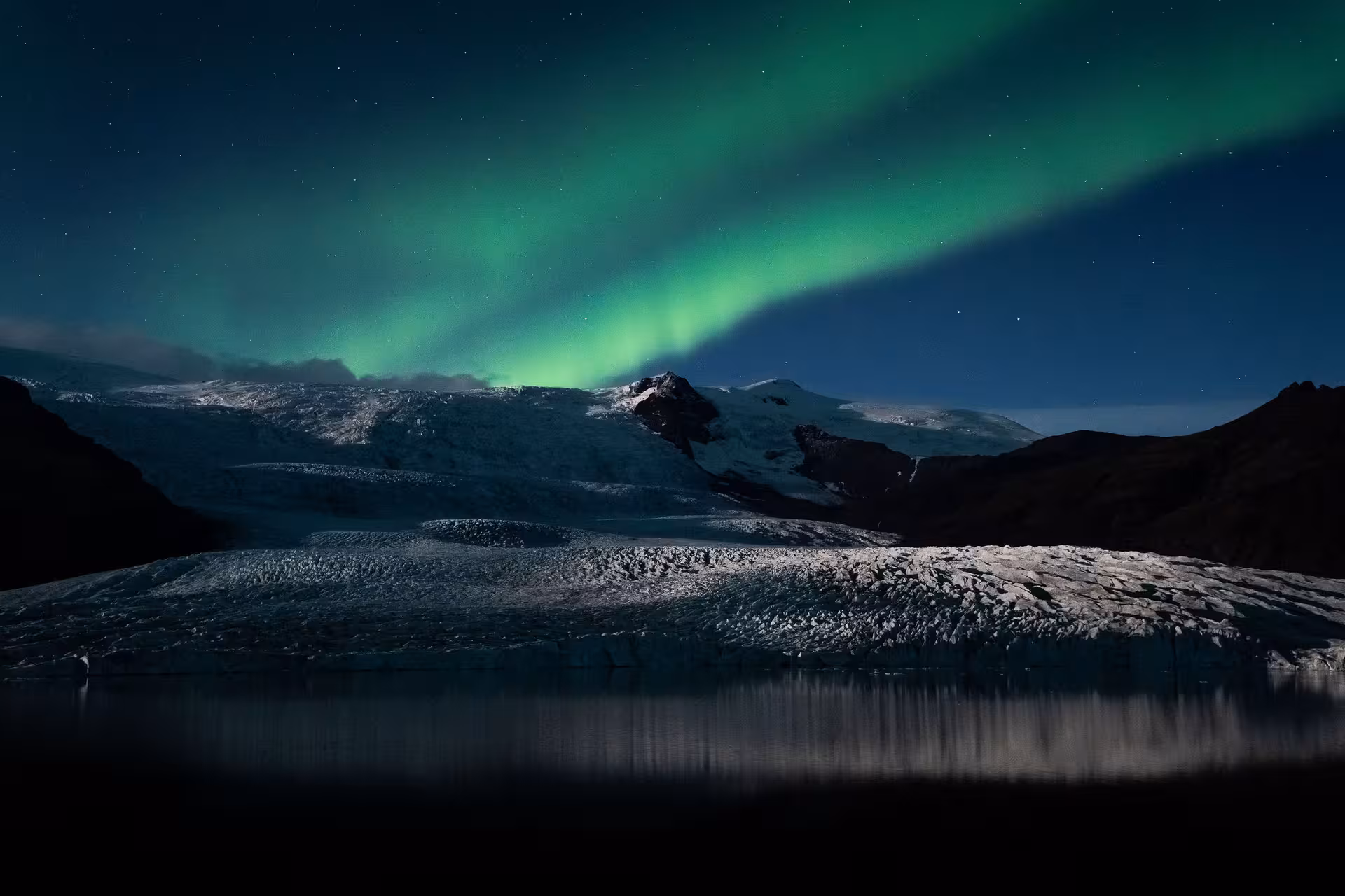 Northern lights aurora borealis glowing green over snowy glacier and dark lake in Iceland at night
