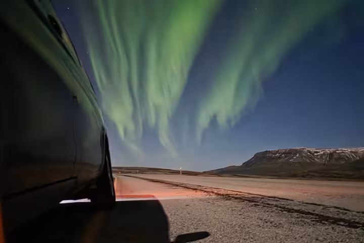 Aurora borealis northern lights over Iceland highway with mountain backdrop at night