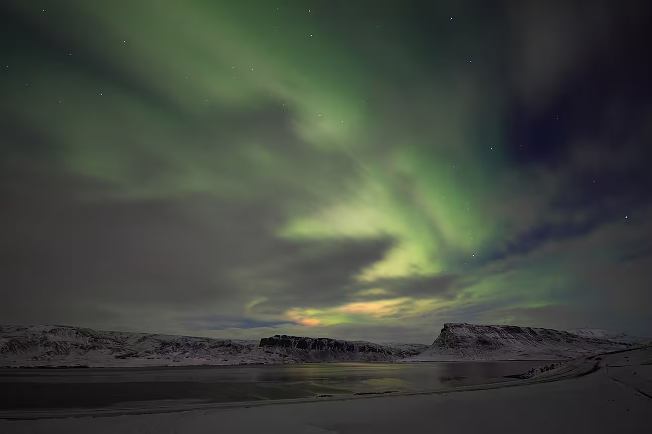 Northern lights dancing over snowy mountains and frozen lake near Reykjavik, Iceland
