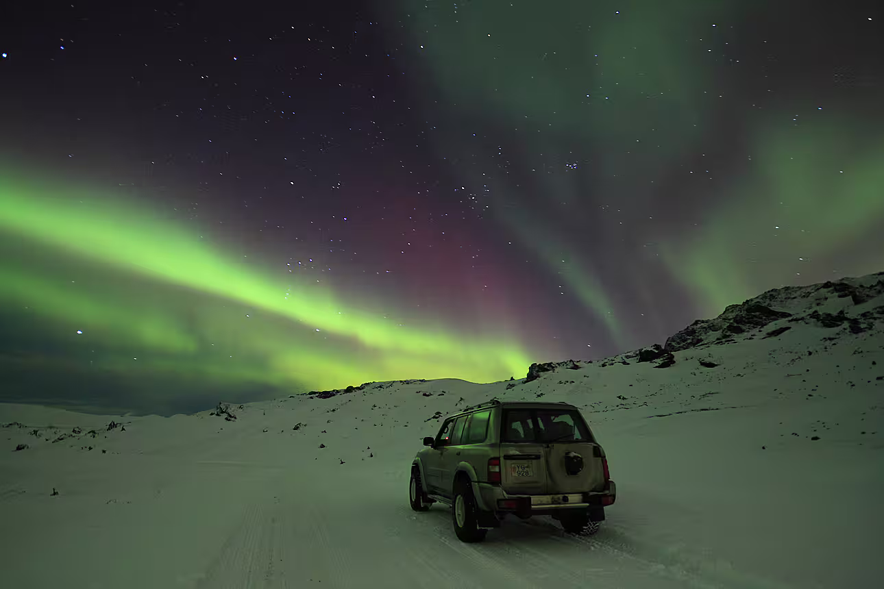 SUV parked on snowy landscape under vivid green and purple northern lights in Iceland