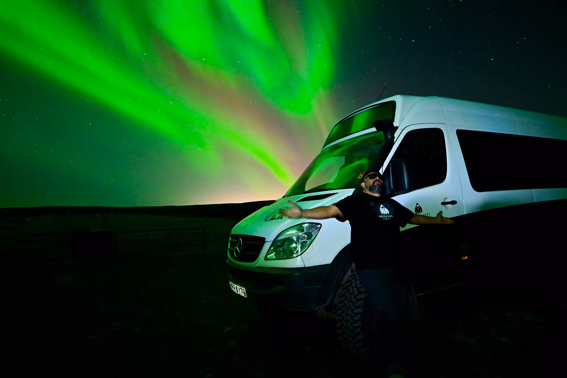 Expert northern lights guide posing beside a 4x4 vehicle under vivid green aurora borealis in Iceland