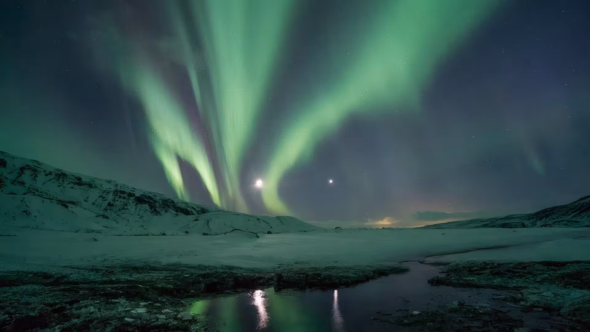 Vivid green northern lights aurora borealis over snowy Iceland landscape with reflective water at night