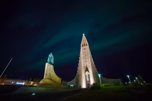 Hallgrímskirkja church illuminated at night with northern lights glowing green over Reykjavik sky