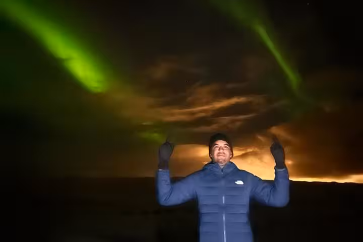 Tourist pointing at vivid green northern lights aurora borealis in night sky near Reykjavik Iceland