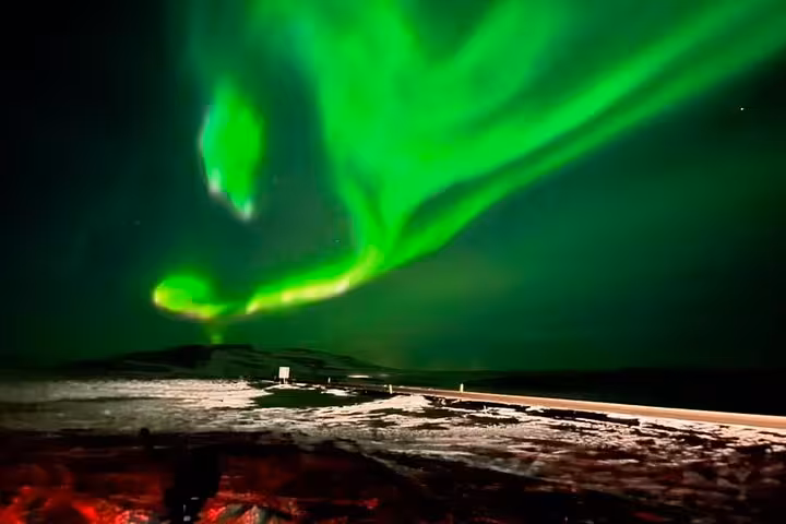 Vivid green northern lights swirling over a snowy Reykjavik landscape at night