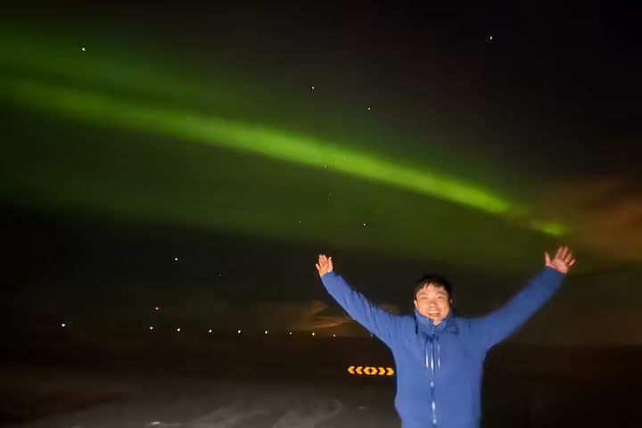 Excited traveler with arms raised under vibrant green northern lights in Reykjavik night sky