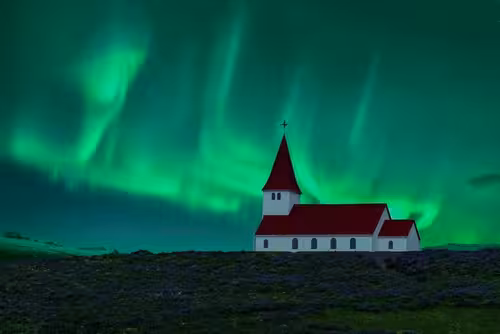 White church with red roof under vivid green northern lights in Iceland night sky