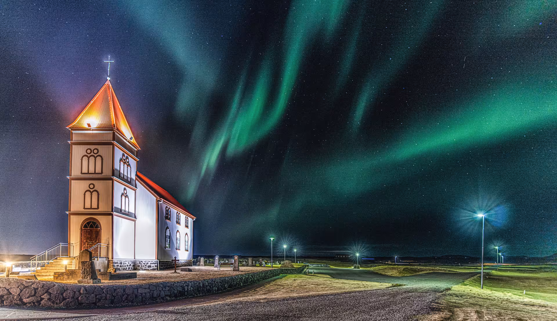 Northern lights dancing over illuminated white church with red roof in Iceland night sky