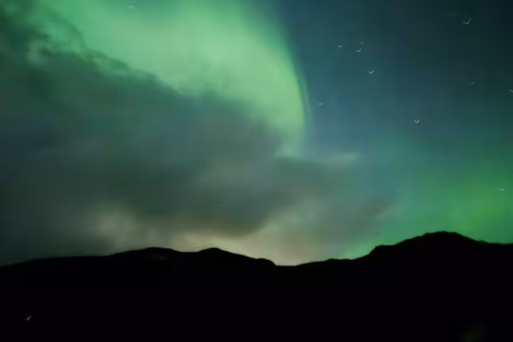 Vivid green northern lights swirling over dark mountain silhouettes in Iceland night sky