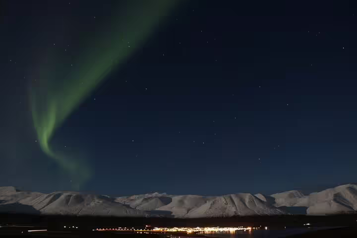 Northern lights dancing over snow-capped mountains and illuminated Icelandic town at night