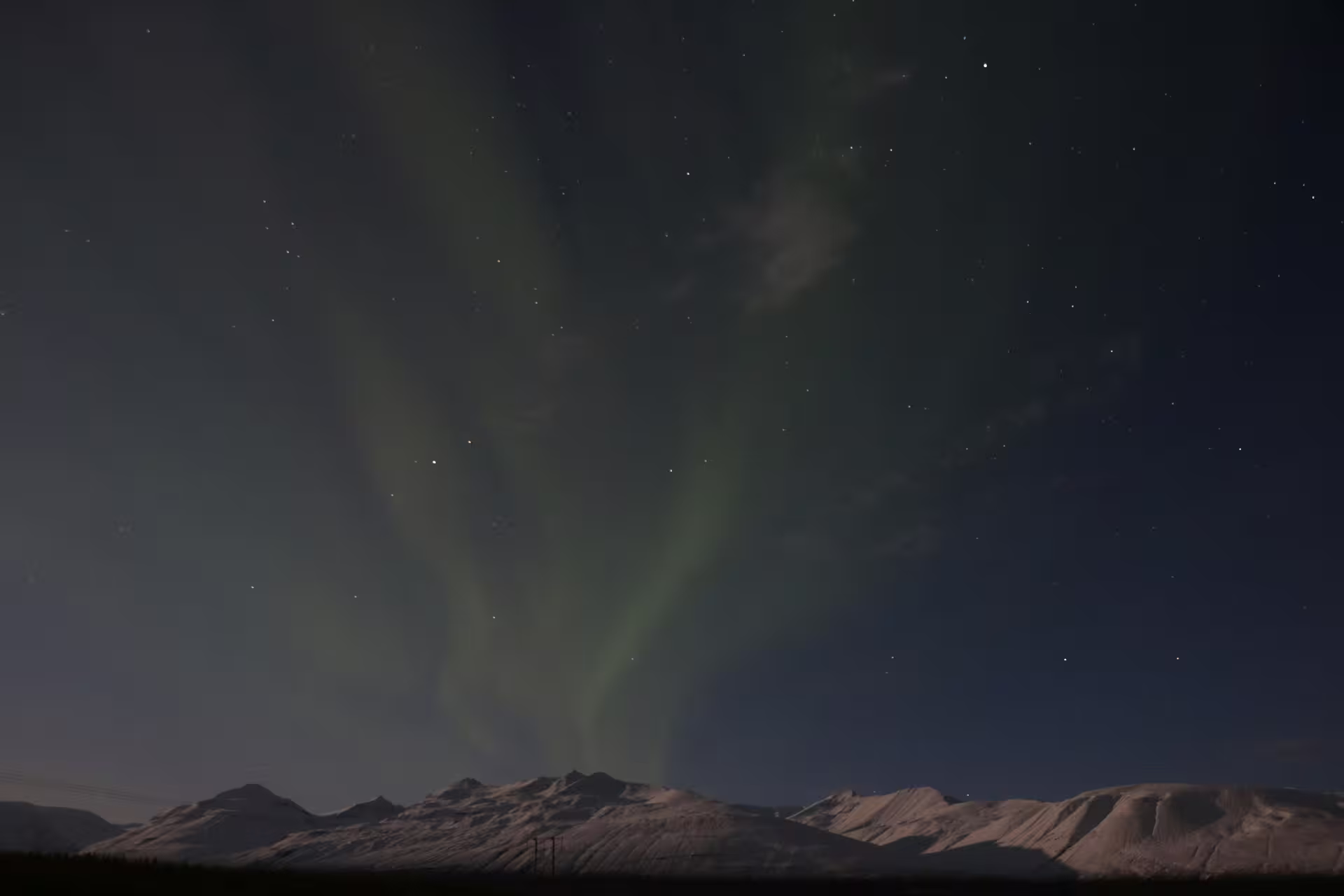Northern lights glowing green over snow-capped mountains in Iceland at night