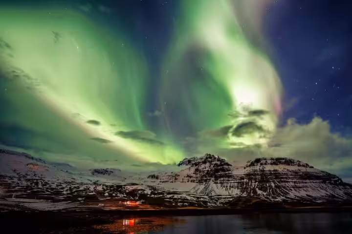 Vibrant green northern lights swirling over snow-capped mountains in Iceland at night