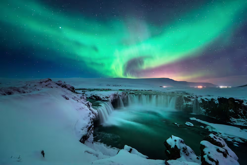 Aurora borealis swirling over a snow-covered waterfall in Iceland on a clear night