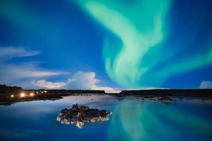 Aurora borealis dancing over calm reflective lagoon near Keflavik Iceland at night