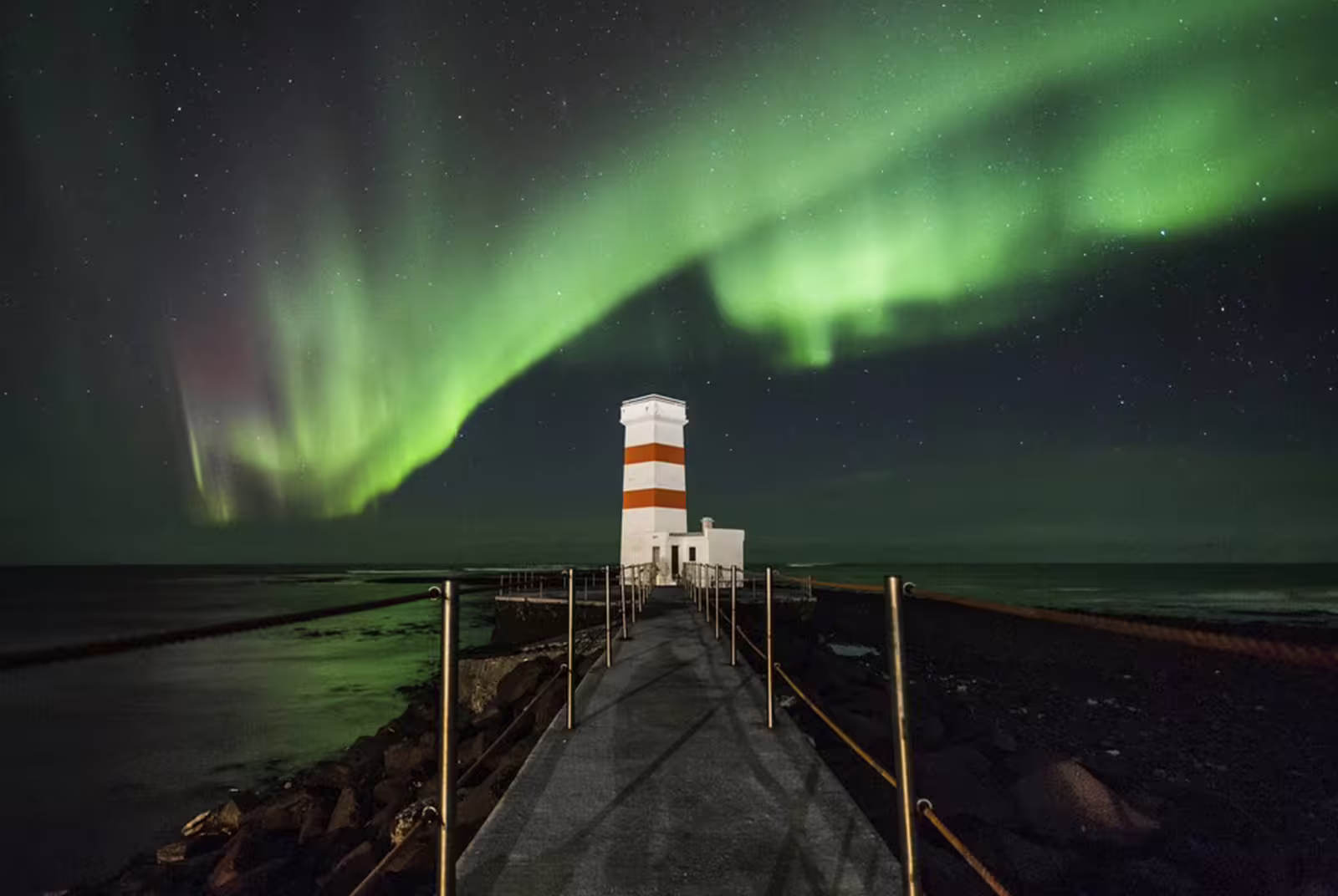 Northern lights aurora borealis over a red and white striped lighthouse on the Reykjavik coastline at night