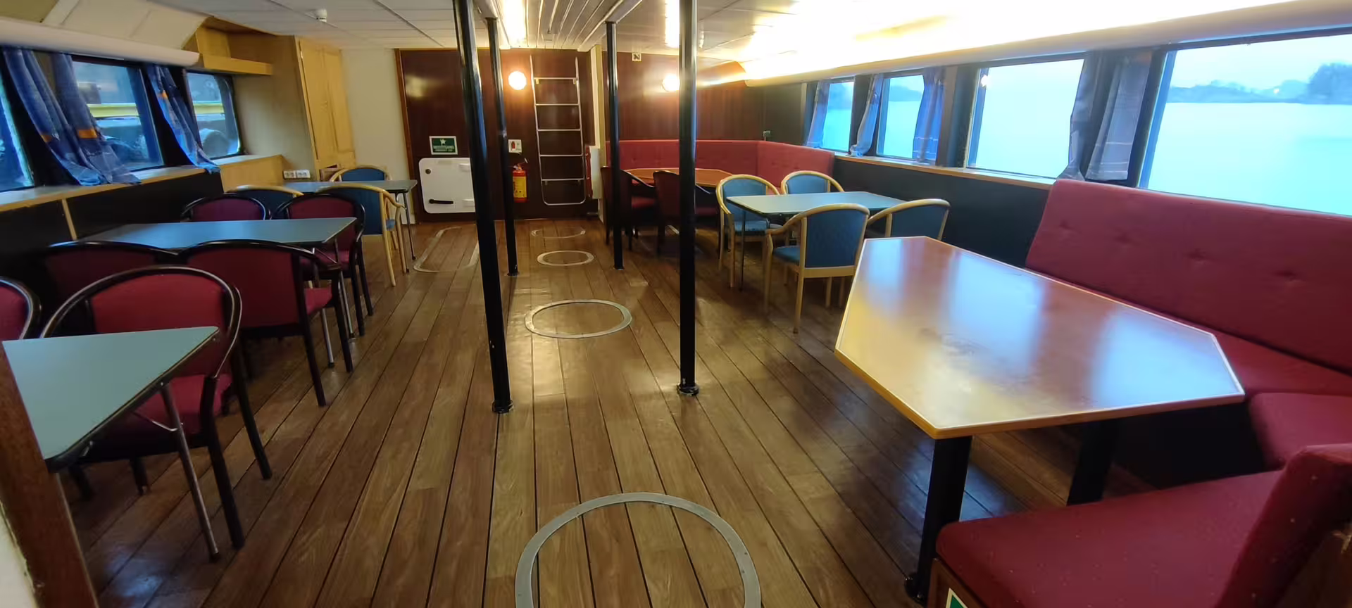 Spacious indoor passenger lounge on a Northern Lights boat tour vessel with wooden deck flooring and panoramic windows