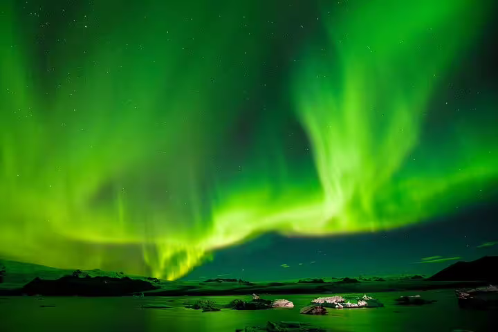 Vibrant green northern lights aurora borealis dancing over a calm glacial lagoon in Iceland at night