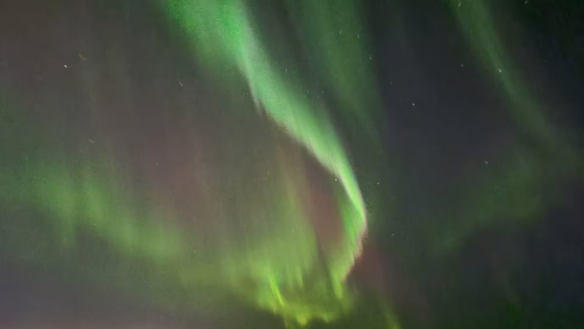 Vivid green northern lights swirling across a dark night sky over Reykjavik waters