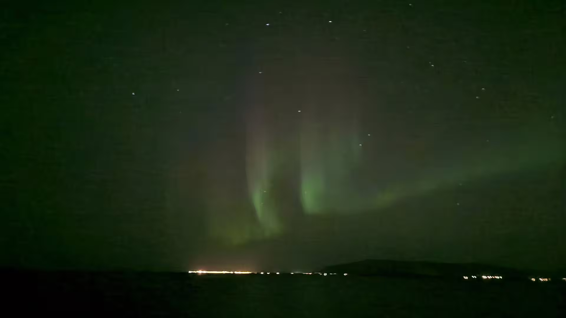 Vibrant green northern lights aurora borealis dancing over dark Reykjavik horizon at night