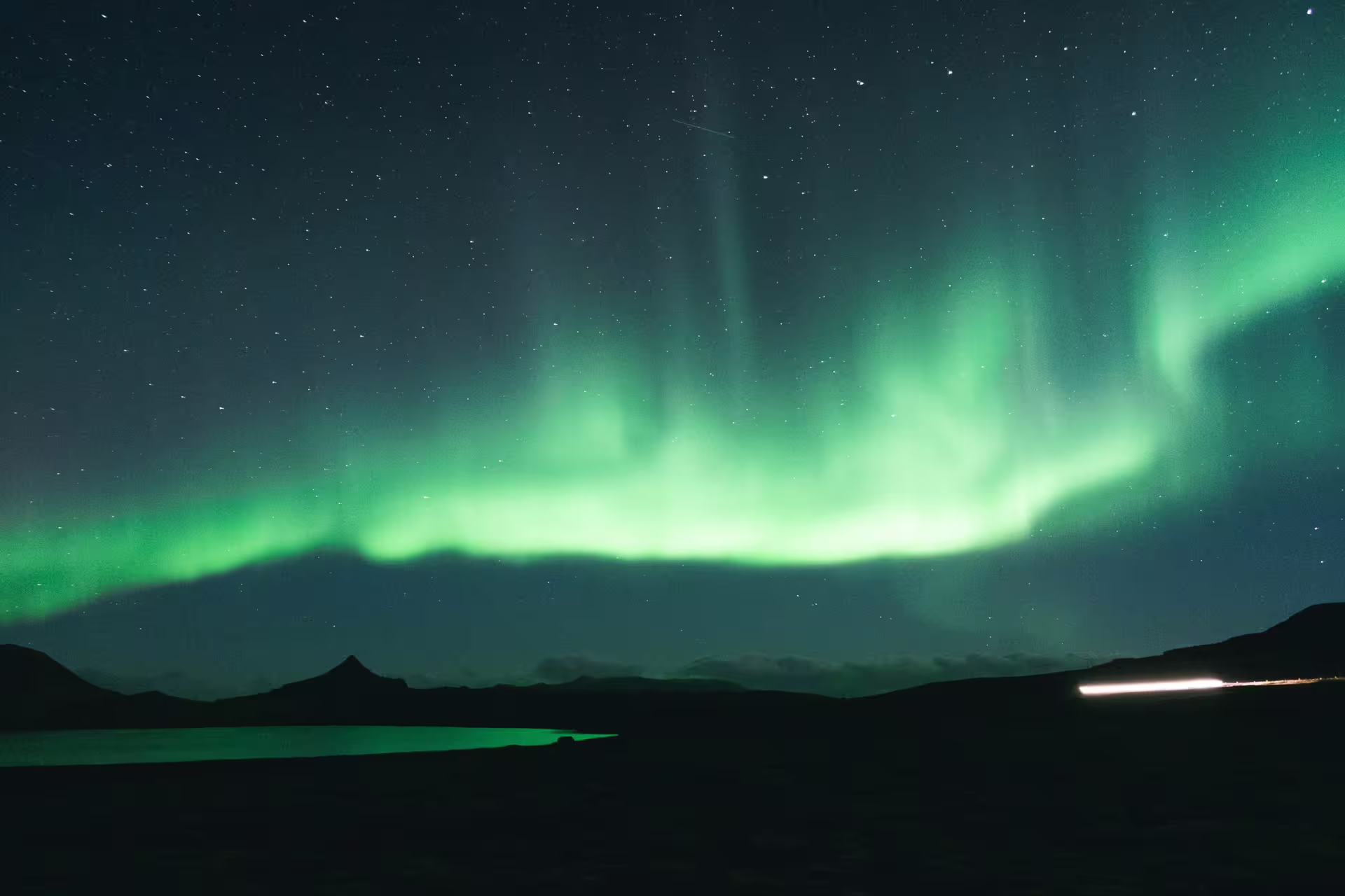 Vivid green northern lights aurora borealis dancing over a calm lake and mountain silhouettes in Iceland