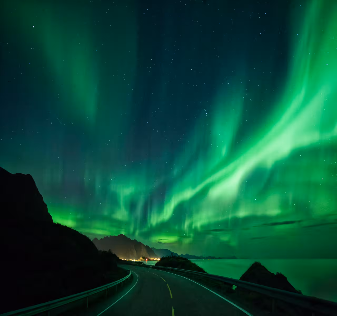 Vibrant green aurora borealis dancing over a winding road in Iceland at night