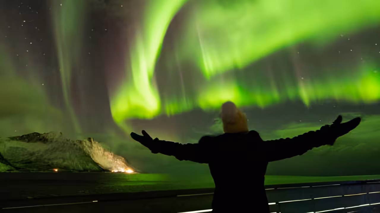 Traveler with arms wide open beneath a spectacular green aurora borealis arch on a private 4x4 Iceland tour