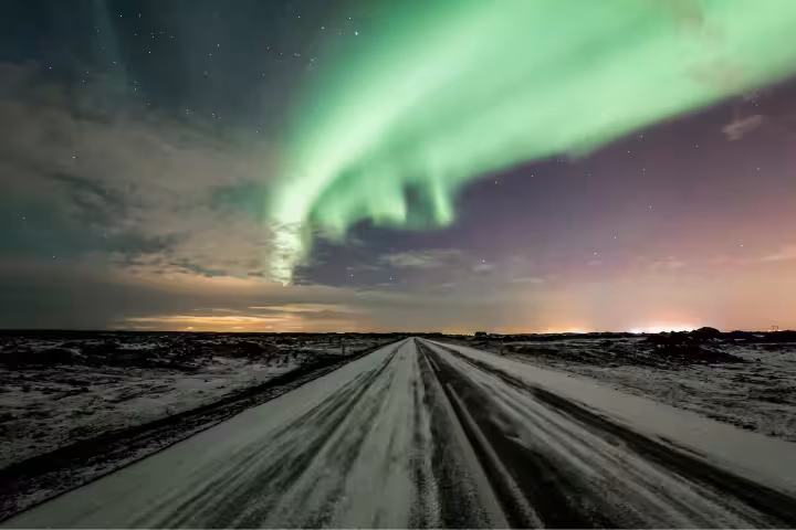 Northern lights swirling over a snowy road at night in Iceland