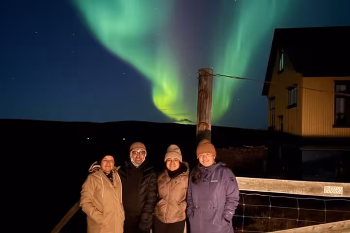 Four tourists posing under vibrant green northern lights aurora borealis at night in Iceland